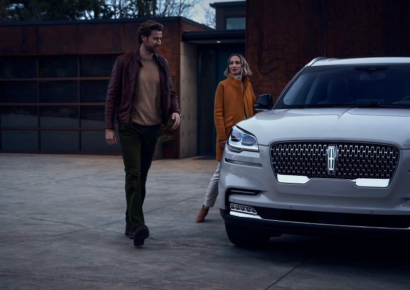 A man and a woman approaching a 2024 Lincoln Aviator® SUV, which illuminates certain lights when they are close | Kindle Lincoln in Cape May Court House NJ